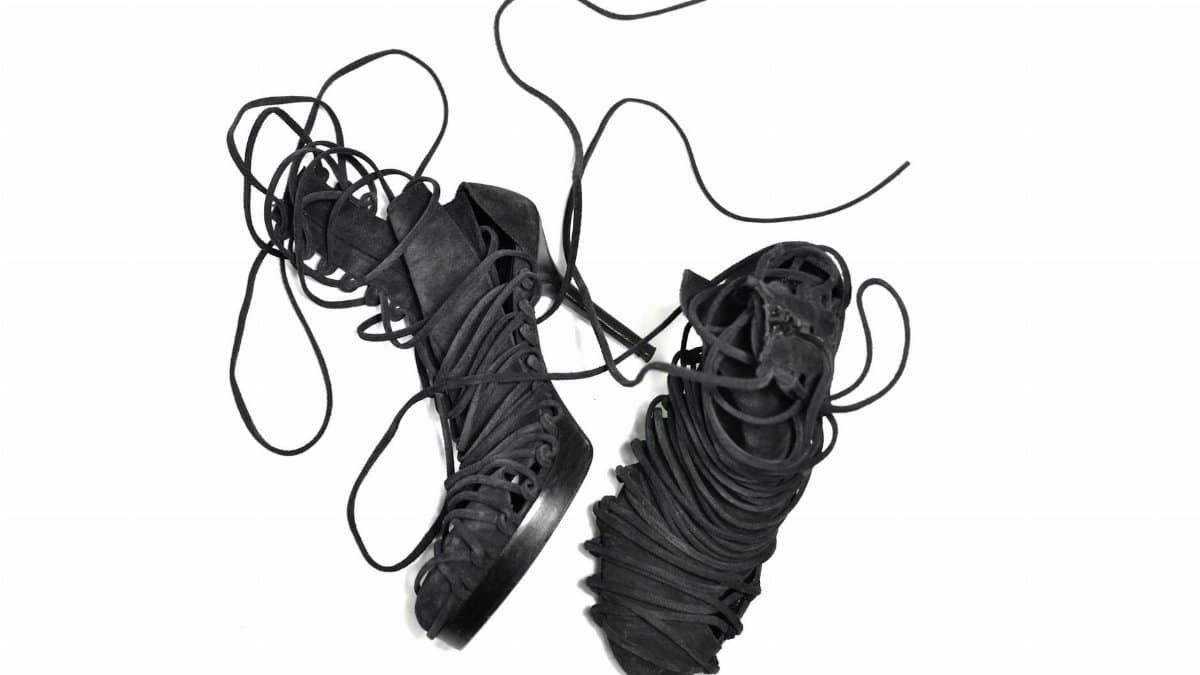 Pair of stylish black lace-up high-heeled boots on a white background showcasing intricate laces.