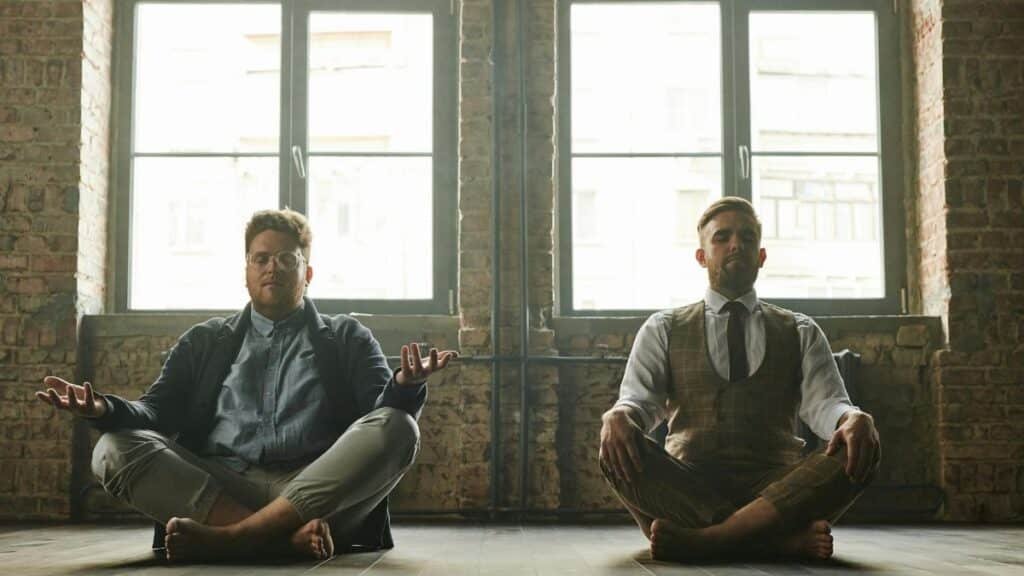 Two men meditating indoors in a loft with natural light, promoting relaxation and mindfulness.