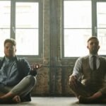 Two men meditating indoors in a loft with natural light, promoting relaxation and mindfulness.