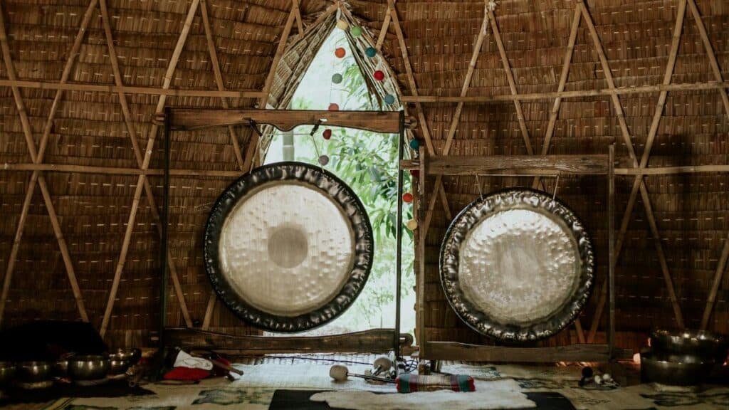 Interior view of a bamboo hut featuring traditional gongs used for sound healing and meditation.