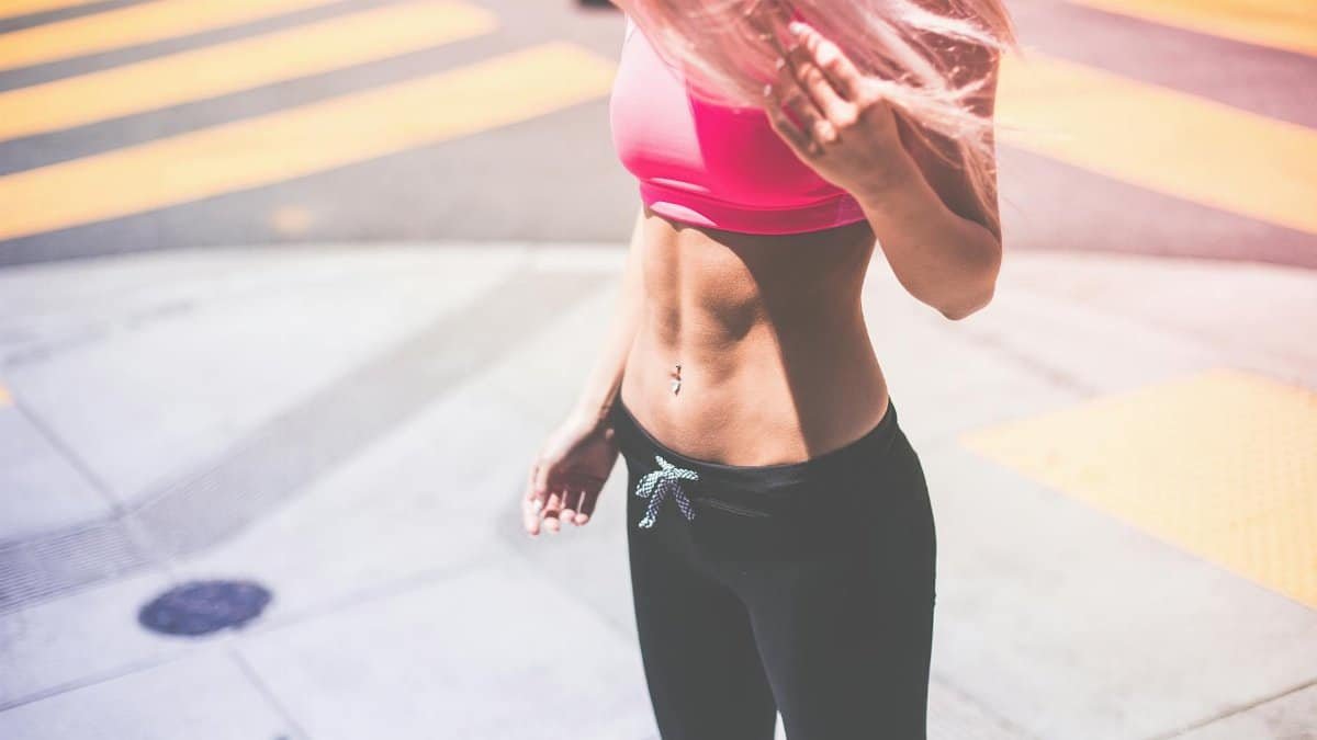 Athletic woman in pink activewear showing toned abs in urban San Francisco setting.