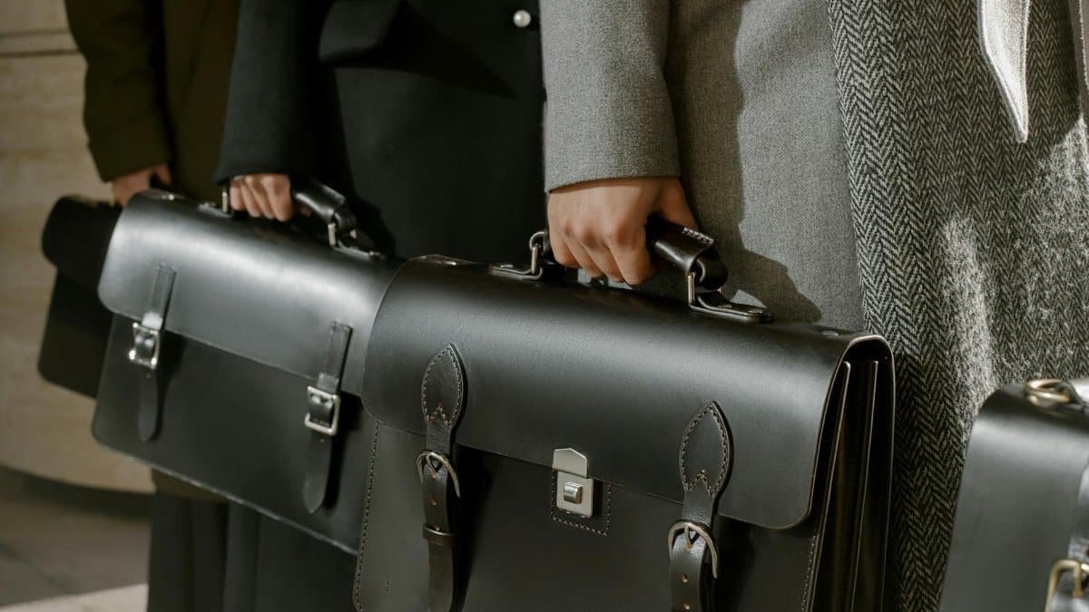 Group of adults holding sleek leather briefcases in formal business attire, emphasizing corporate professionalism.