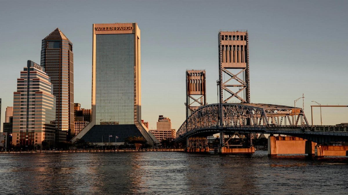 Stunning view of Jacksonville, FL skyline at sunset with iconic bridges and modern skyscrapers reflecting on the water.