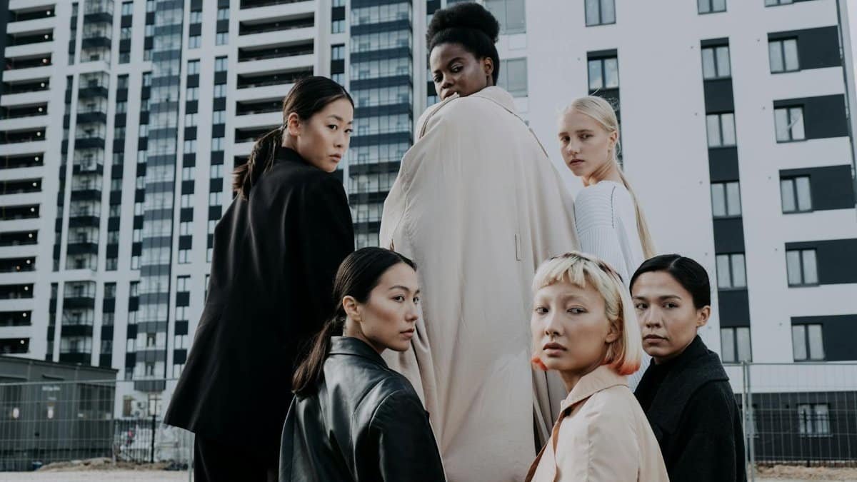 Group of diverse women modeling fashion in a modern urban setting with high-rise buildings.
