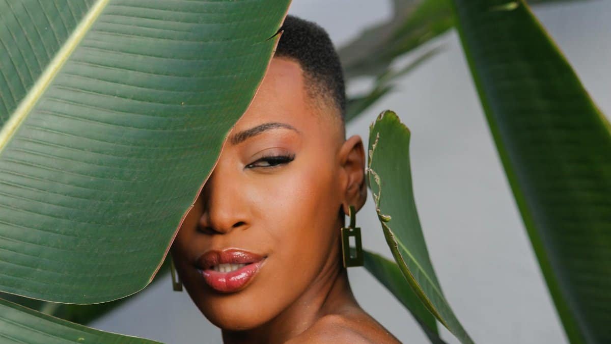 Beautiful portrait of a woman partially hidden behind lush tropical leaves.