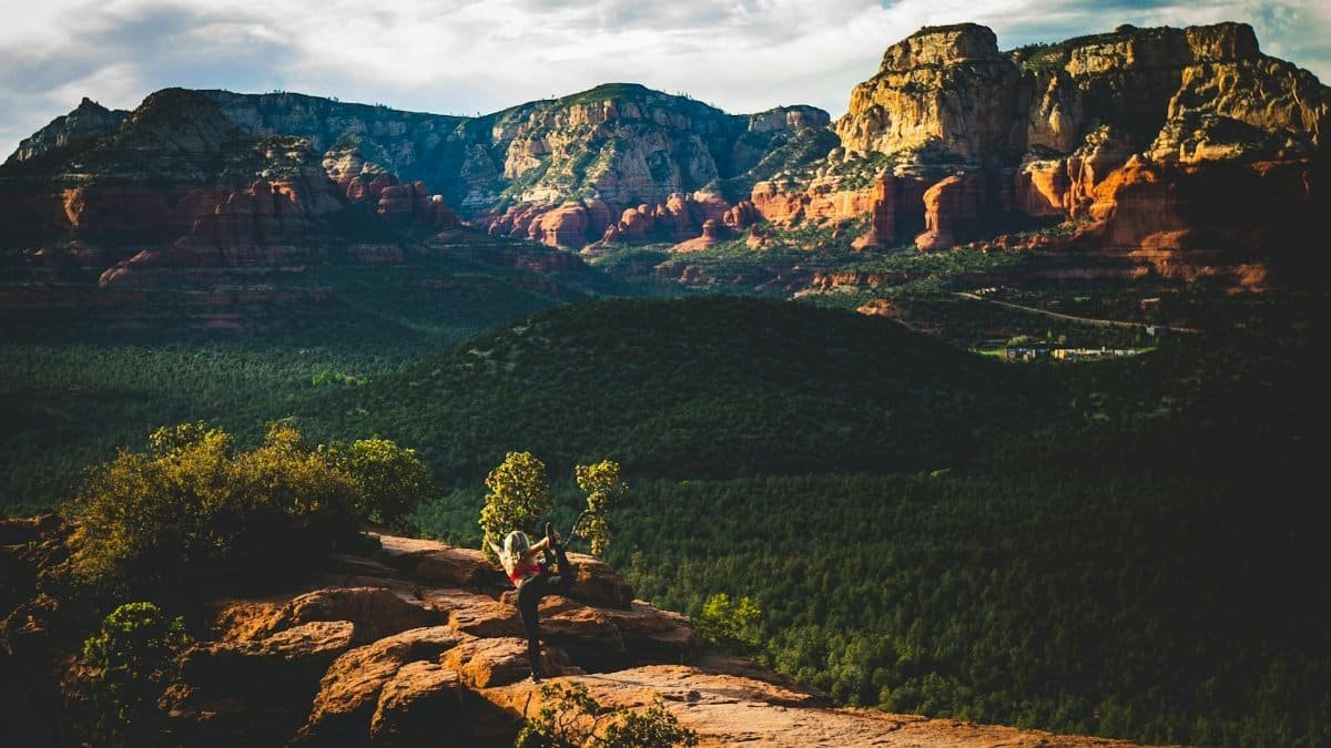 Woman performing yoga pose on a rocky ledge against the stunning Sedona landscape during sunset.