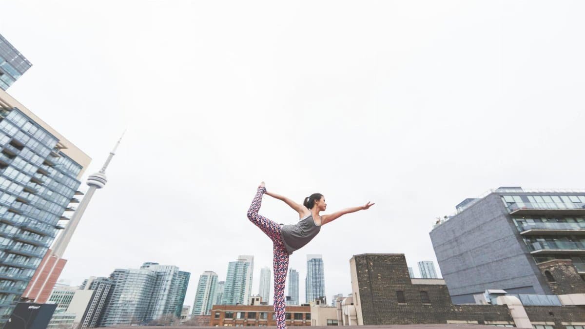 A woman performs yoga on a rooftop overlooking a modern city skyline, embodying balance and urban tranquility.