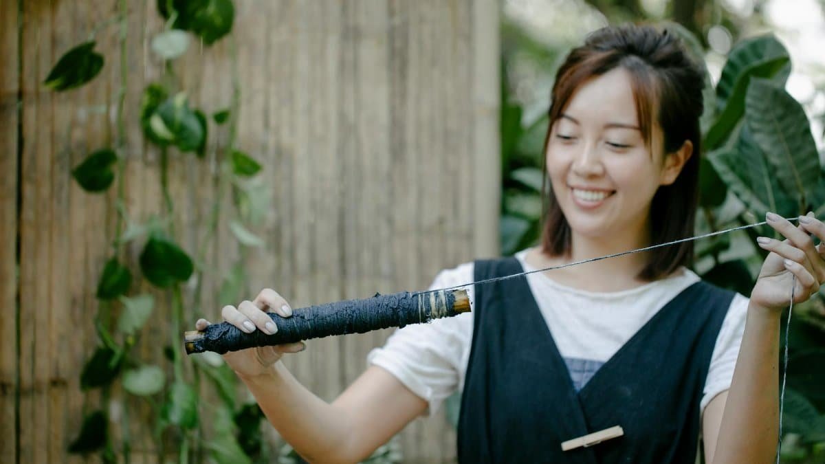 Smiling young woman enjoying her shibori dye crafting in a garden setting, showcasing creativity and traditional techniques.