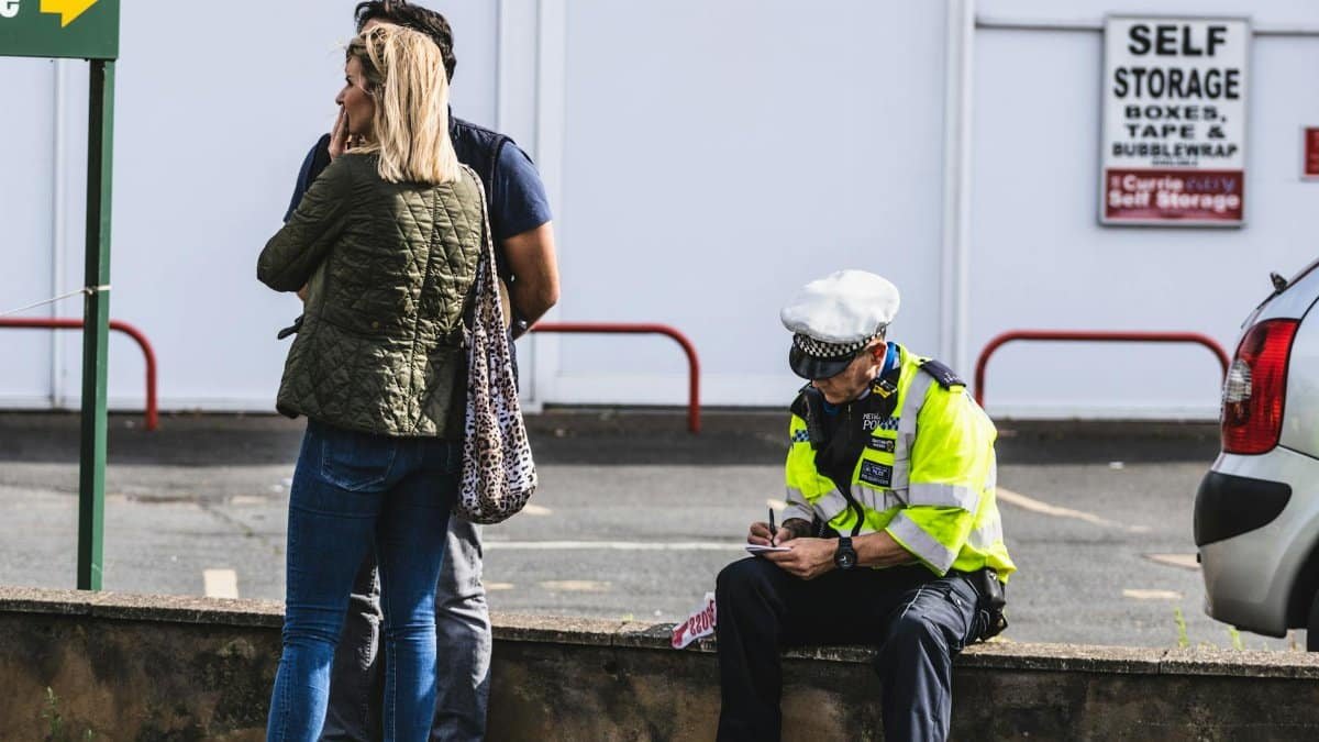 Police officer writing a ticket near a self-storage area with people in the background.