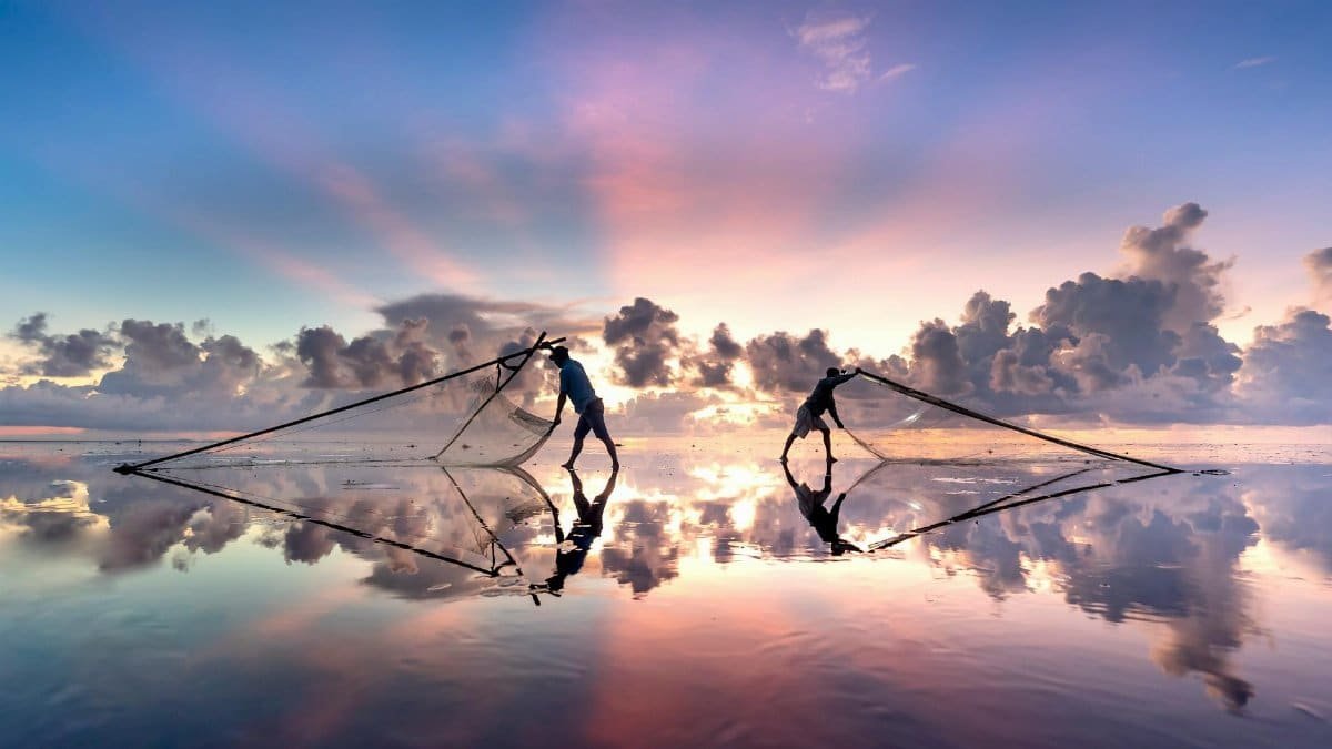 Silhouetted fishermen casting nets during a vivid sunset over tranquil waters.