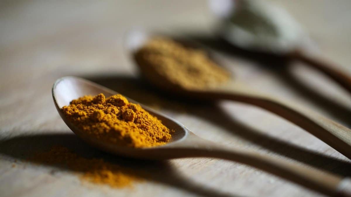Vibrant turmeric powder on a wooden spoon with a blurred background for culinary use.