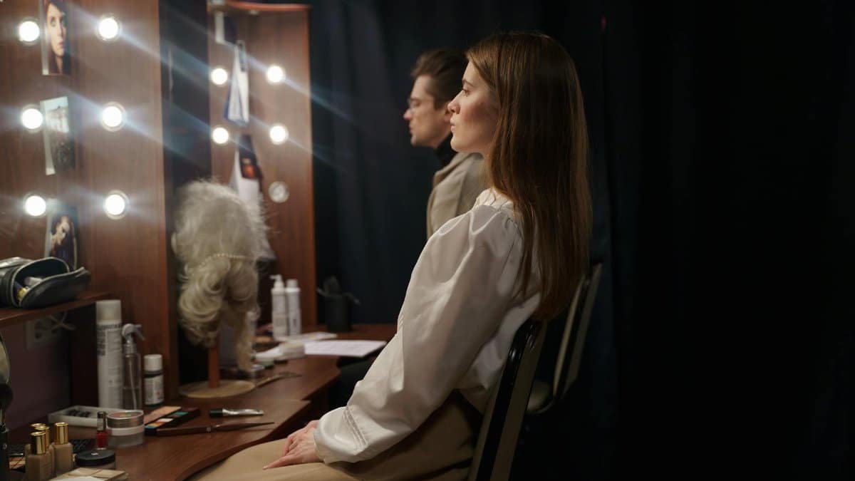 Two actors in a theater dressing room preparing for a performance, sitting and reviewing scripts.