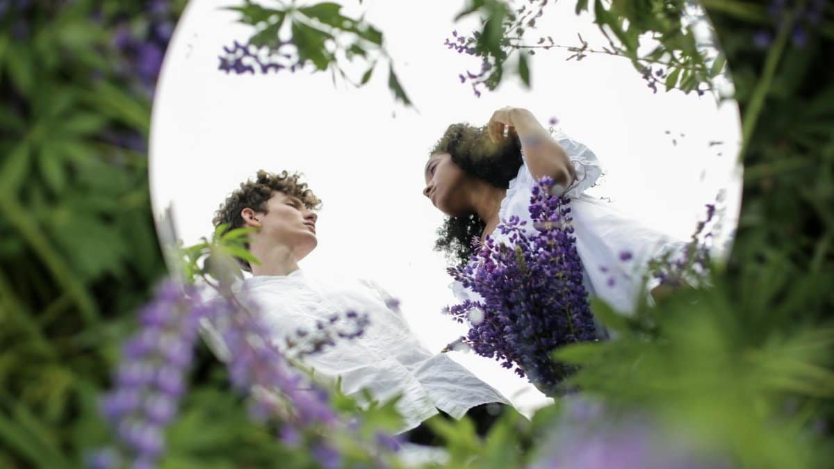 A diverse couple reflected in a mirror surrounded by lupine flowers, symbolizing unity and nature.
