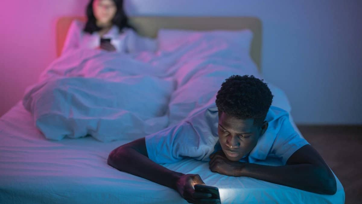 A couple lying in bed using smartphones at night under soft lighting, focusing on technology and connectivity.