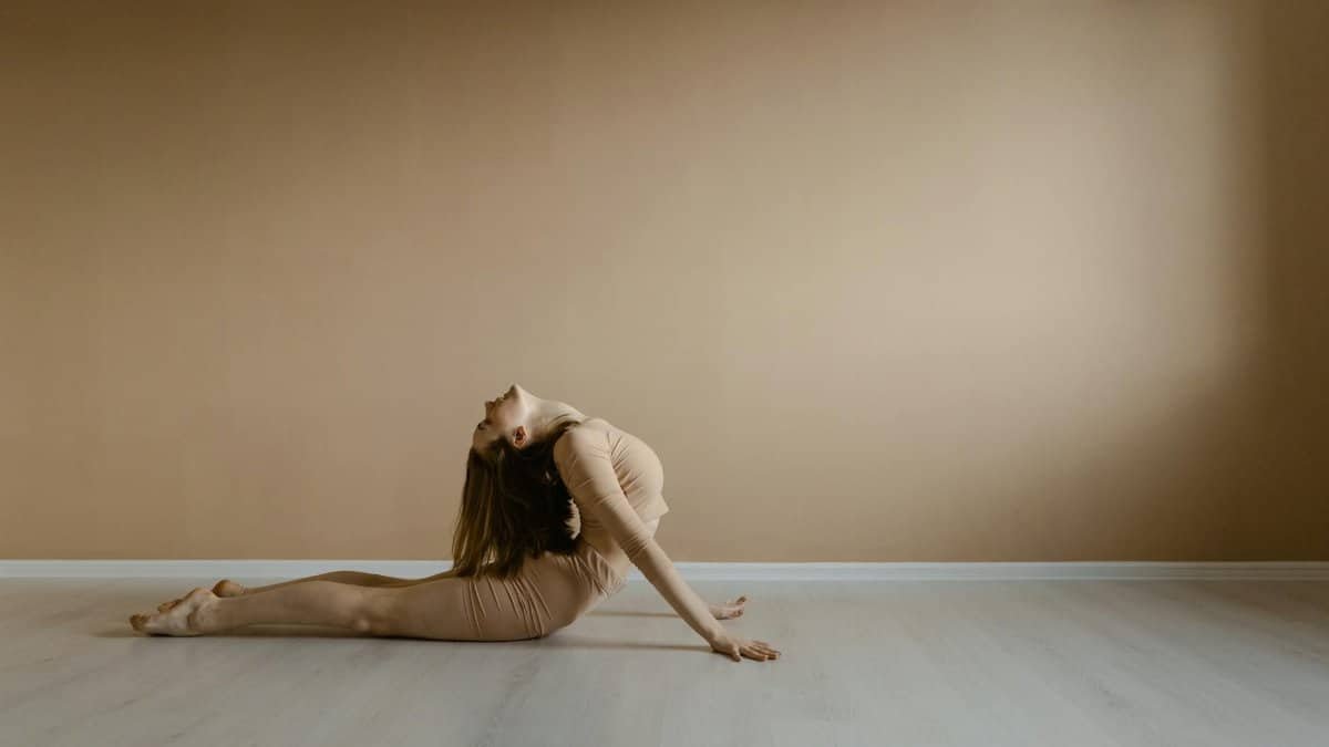 A woman demonstrates a flexible yoga pose in a minimalist indoor environment, embodying peace and balance.