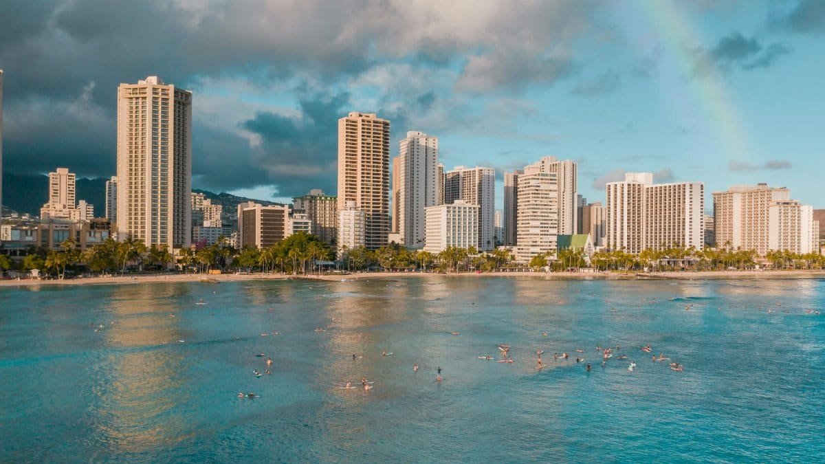 A lively daytime scene of Waikiki Beach with surfers and modern skyscrapers under a bright sky.