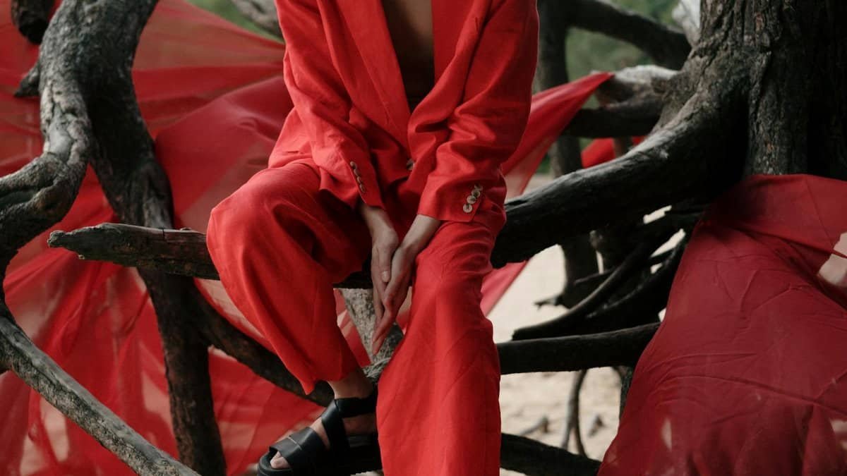 Person in vibrant red suit sitting among twisted tree roots, combining fashion with nature.