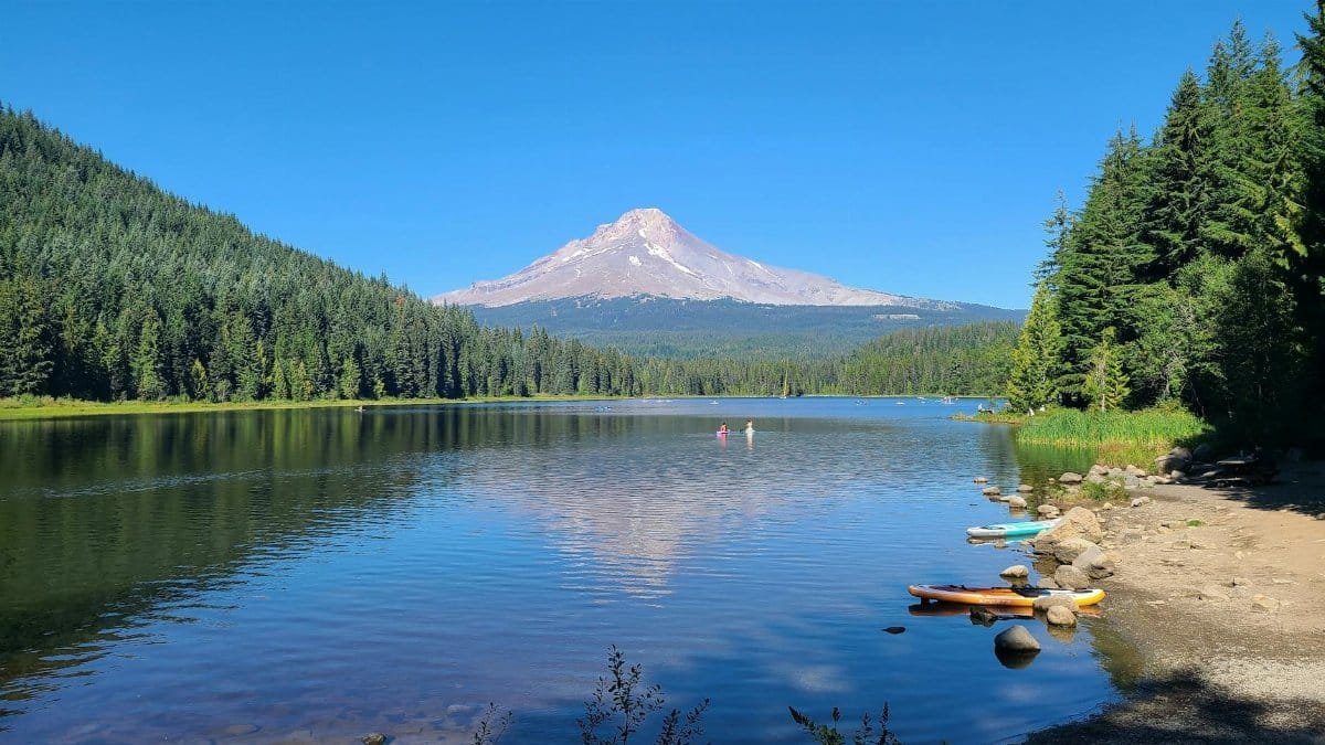 Tranquil summer day at Trillium Lake with a clear view of Mount Hood and kayaks on the shore.