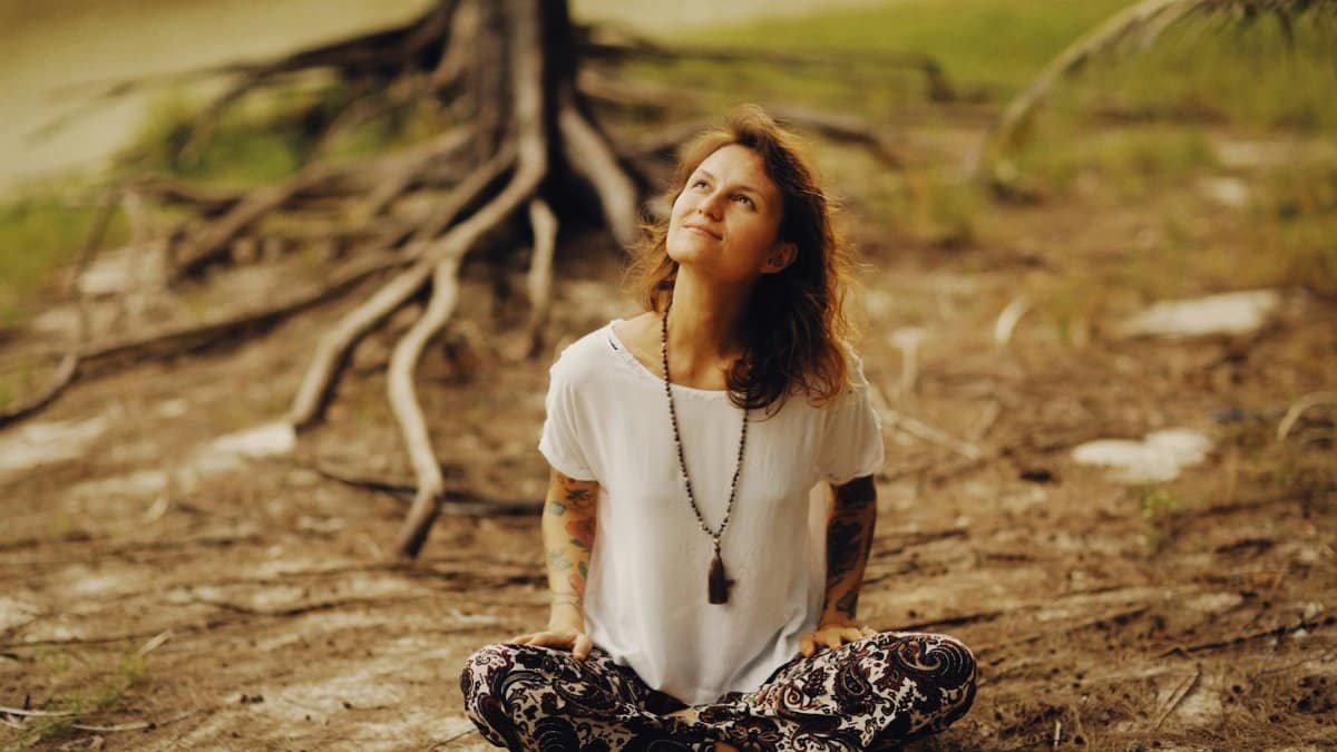 A thoughtful woman in a peaceful meditation pose outdoors, surrounded by nature.