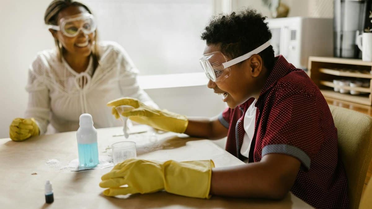 Boy and woman conducting a science experiment at home, wearing gloves and goggles.