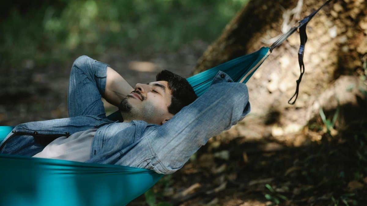 A young man peacefully resting in a hammock outdoors in a serene forest setting.
