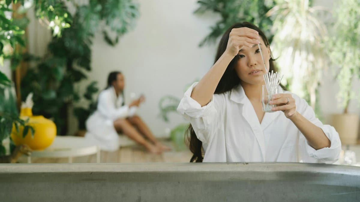 A woman works with glassware in a serene, plant-filled setting, creating a balanced, natural ambiance.