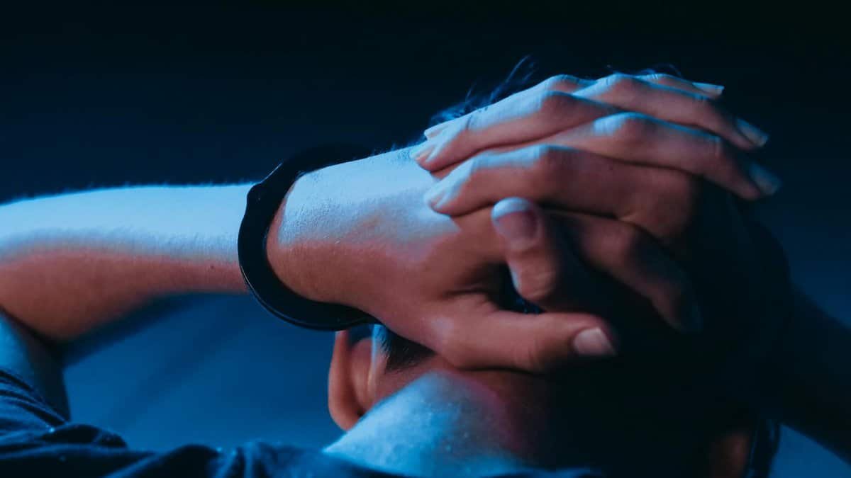 Close-up of a person in handcuffs with hands behind head, conveying themes of arrest and law enforcement.