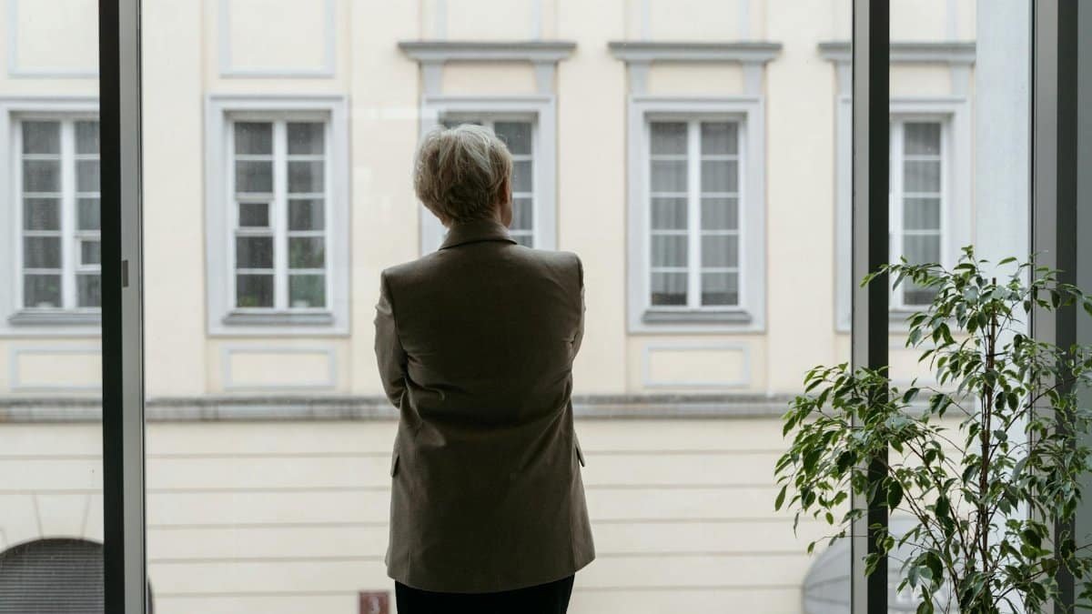 A professional woman gazes thoughtfully through an office window, lost in contemplation.