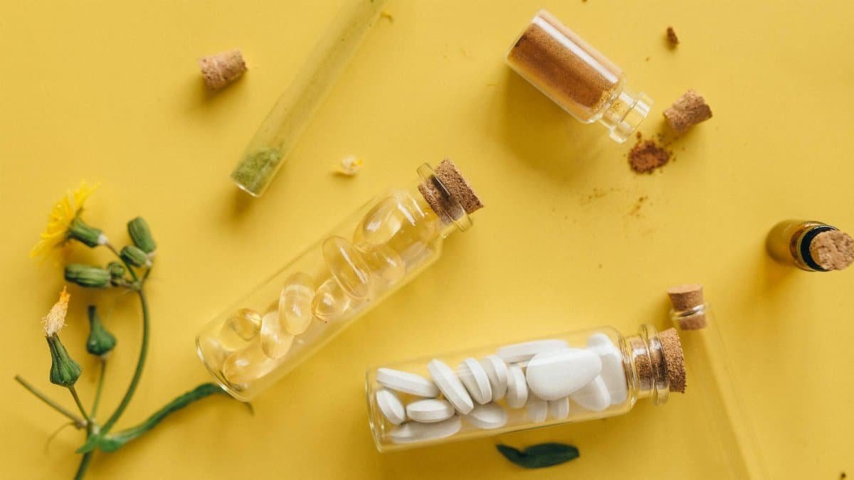Top view of medicinal herbs, pills, and powders in bottles against a vibrant yellow backdrop.