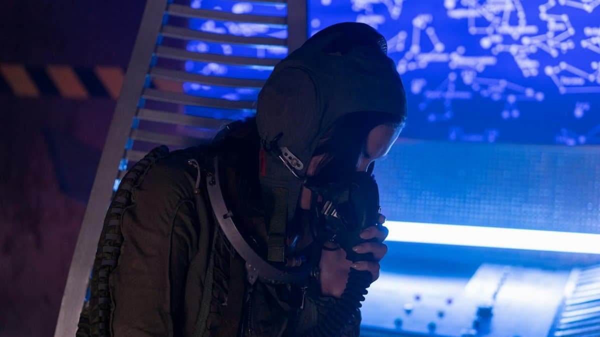 A woman in a spacesuit working in a futuristic control room with a star map.