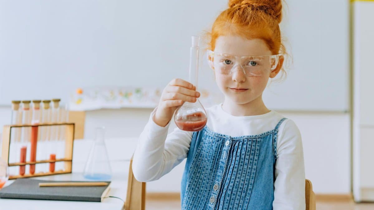 Girl in class conducting a science experiment with safety goggles and a volumetric flask.