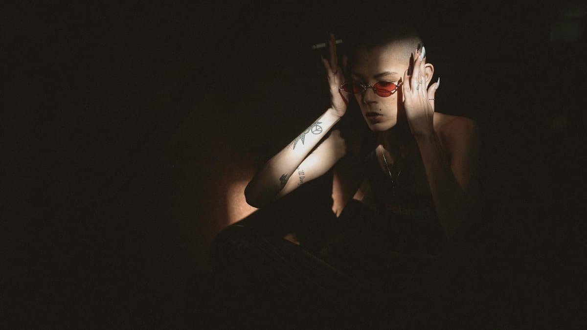Artistic portrait of a tattooed woman with sunglasses smoking in dramatic lighting.