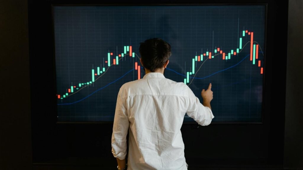 Adult male reviewing stock market data on a large display screen indoors.