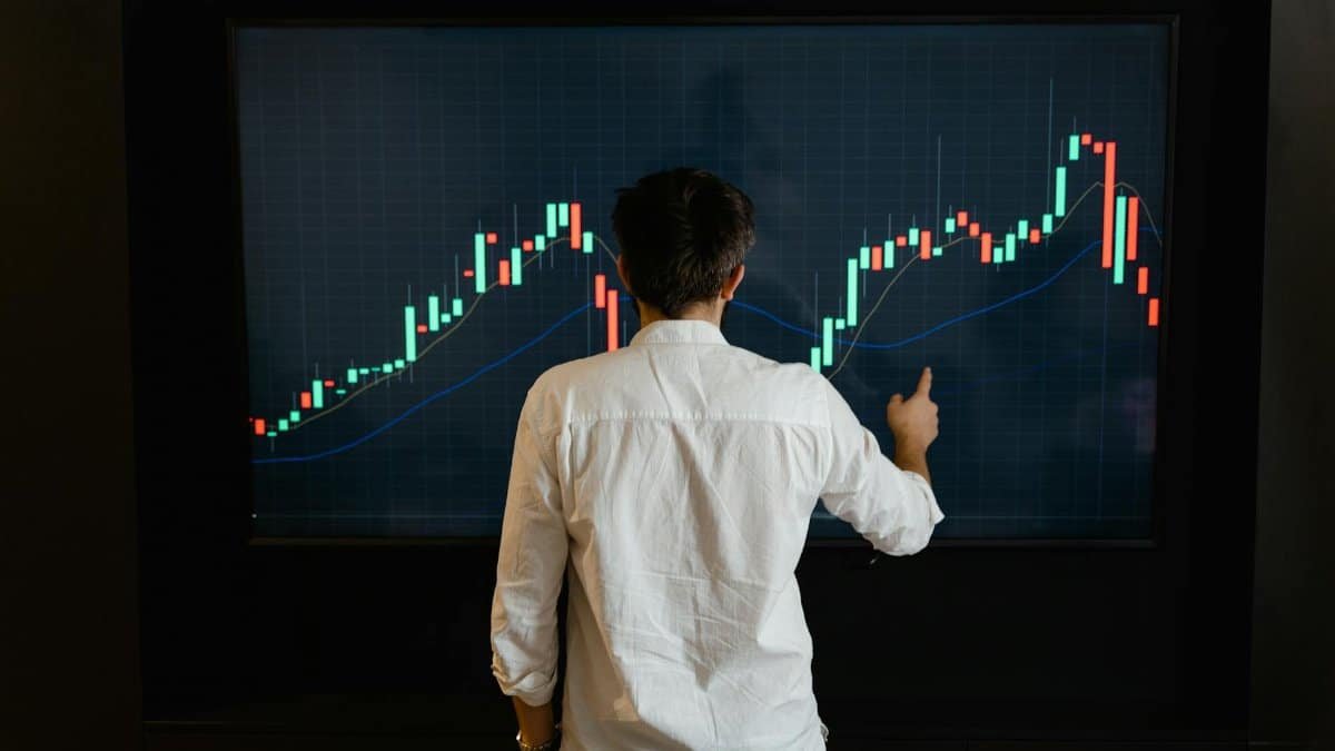 Adult male reviewing stock market data on a large display screen indoors.