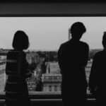 Silhouette of three people viewing Washington DC from a high-rise window at dusk.
