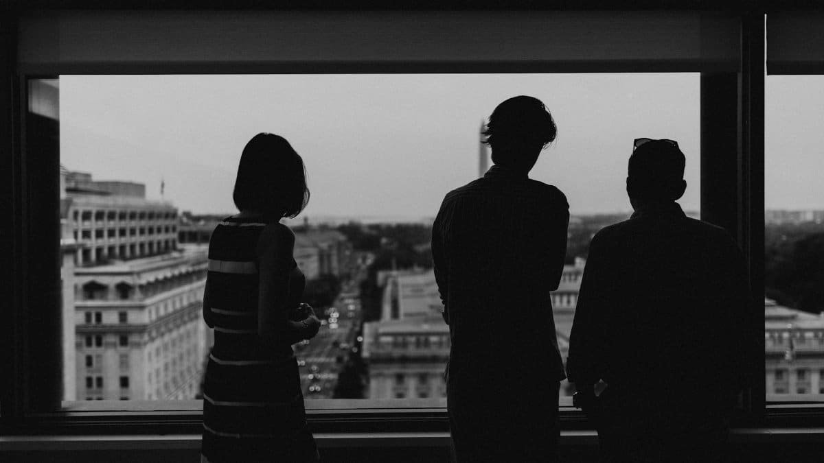Silhouette of three people viewing Washington DC from a high-rise window at dusk.
