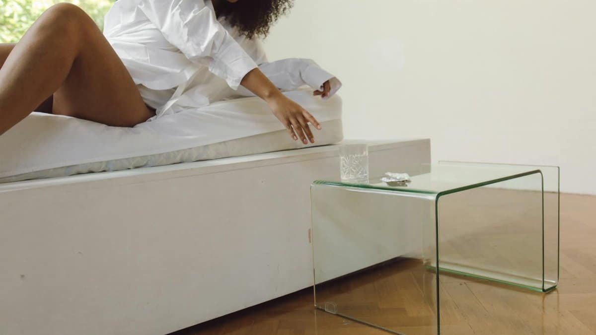 A woman reaches for a glass of water on a minimalistic bedside table.