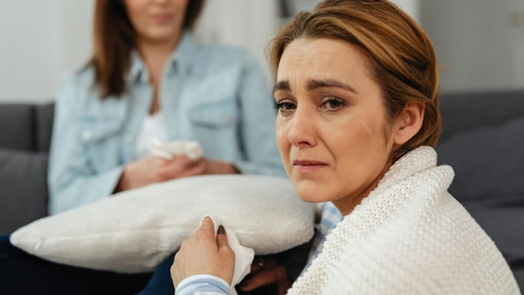 A close-up of a woman in distress being comforted by a friend in a cozy setting.