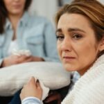 A close-up of a woman in distress being comforted by a friend in a cozy setting.