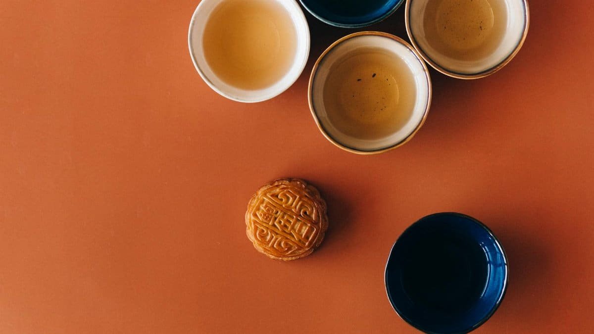 Top view of a traditional tea set with a decorated mooncake on an orange surface.
