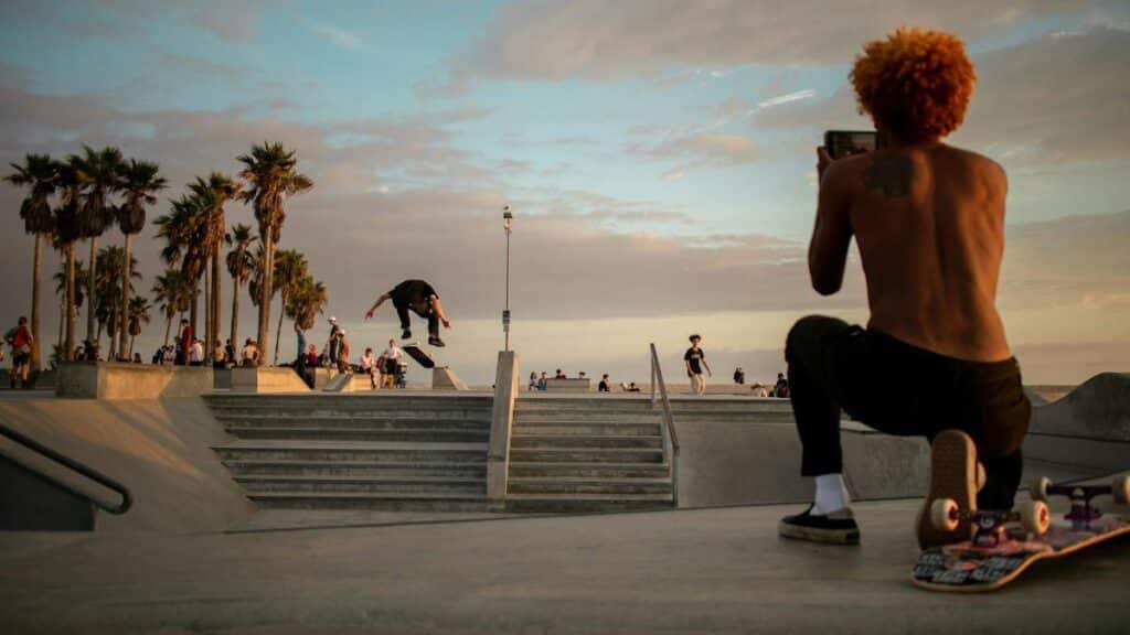 A skateboarder performs a trick at a vibrant skate park in Los Angeles during sunset.