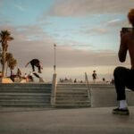 A skateboarder performs a trick at a vibrant skate park in Los Angeles during sunset.