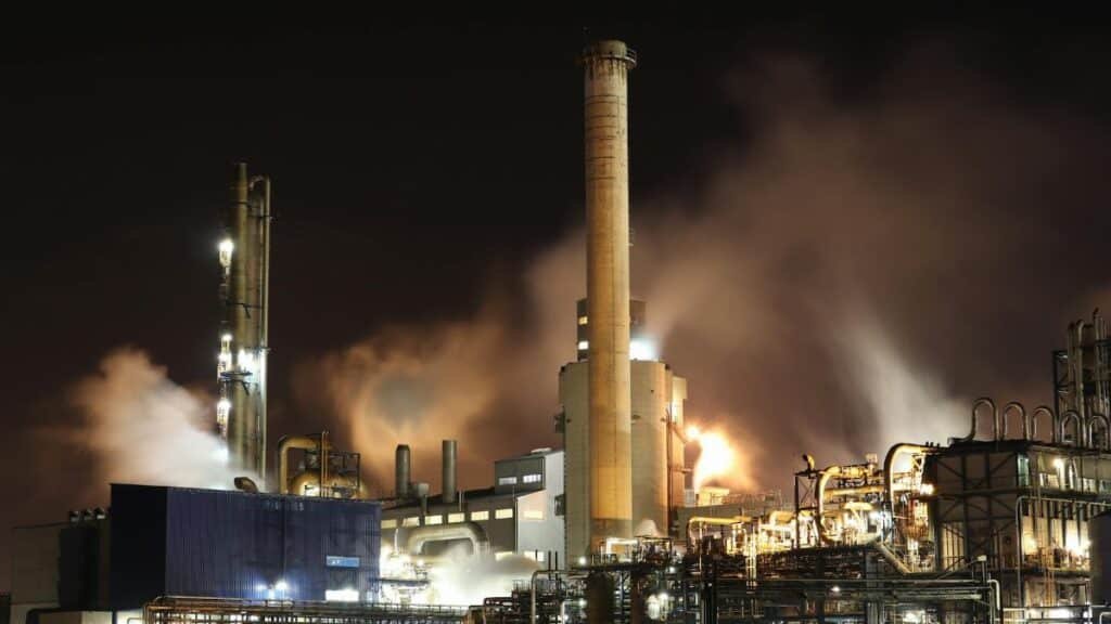 A nighttime view of an industrial factory with smokestacks emitting smoke, highlighting energy production and pollution.