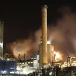A nighttime view of an industrial factory with smokestacks emitting smoke, highlighting energy production and pollution.