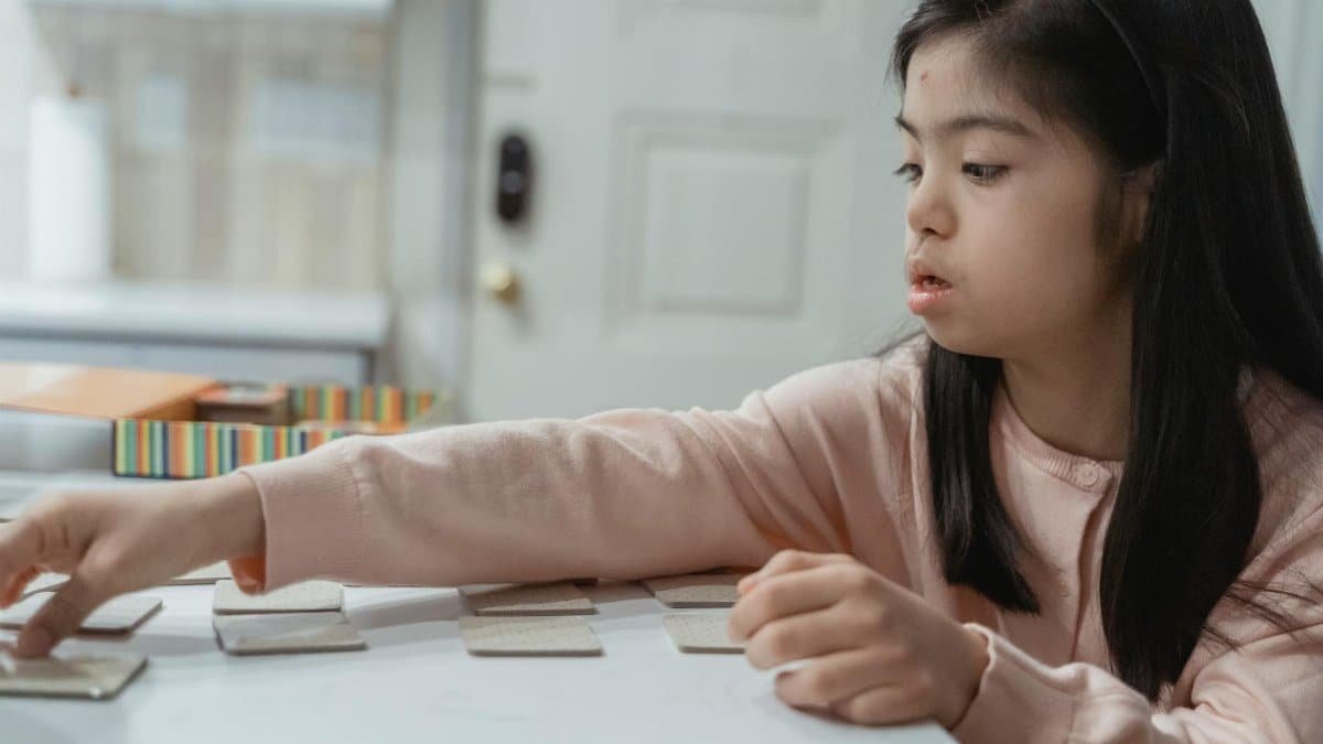 Young Asian girl with Down Syndrome engaged in a game indoors, wearing a pink sweater.