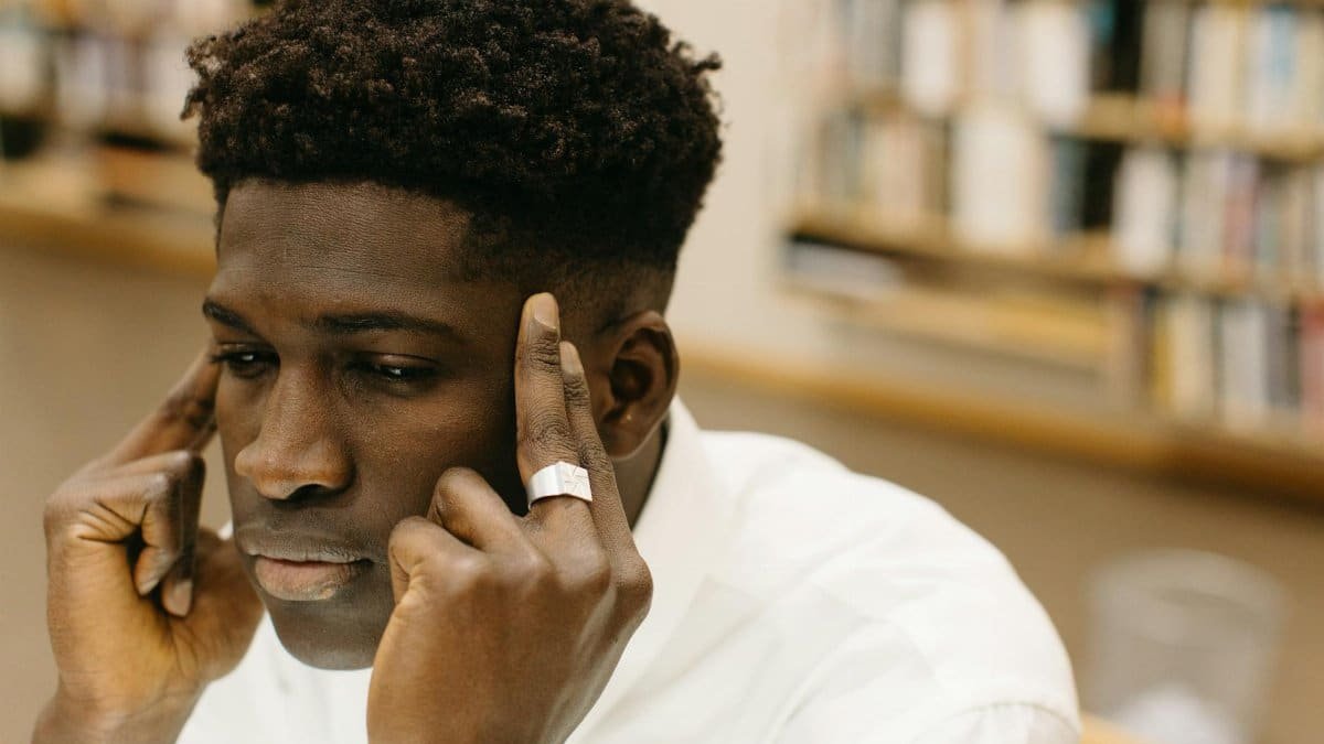 A contemplative man with fingers on temples, pondering in a library.