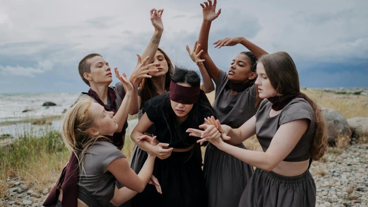 Group of diverse women performing a contemporary dance outdoors on a rocky shoreline.