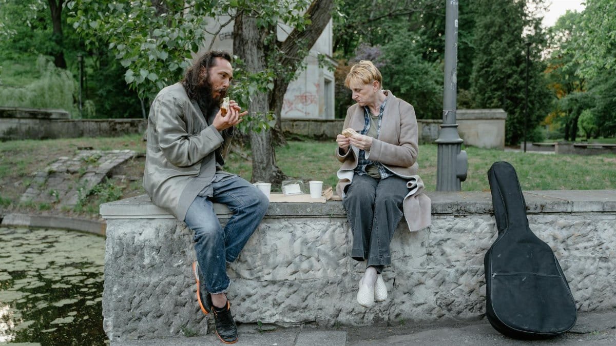 Two individuals sharing a meal outdoors on a stone bench, highlighting companionship and resilience.