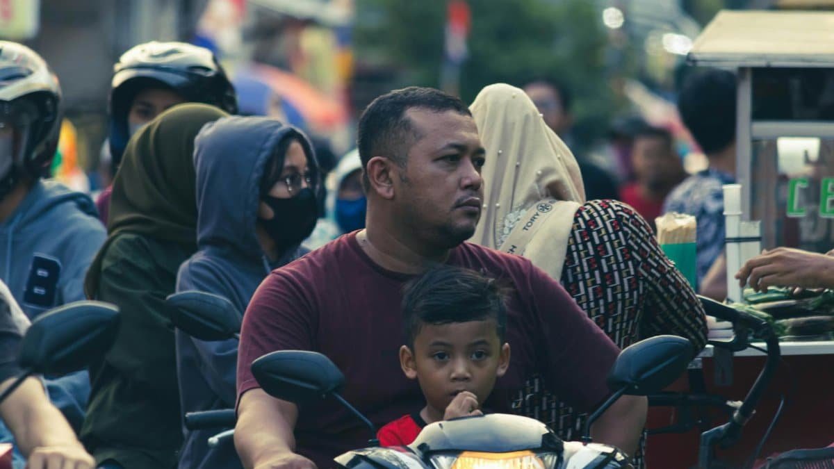 A father and son navigate a crowded street on a motorcycle, highlighting daily urban life.