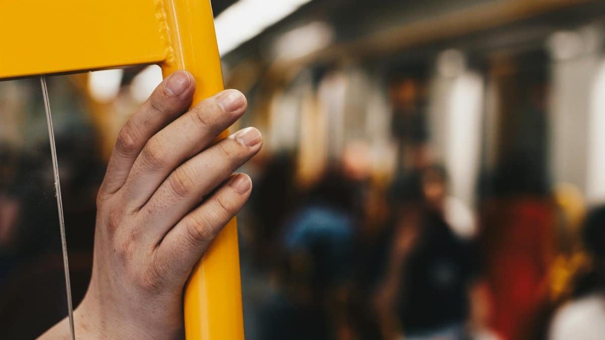 A close shot of a hand holding onto a yellow bar inside a busy metro train, evoking city life.